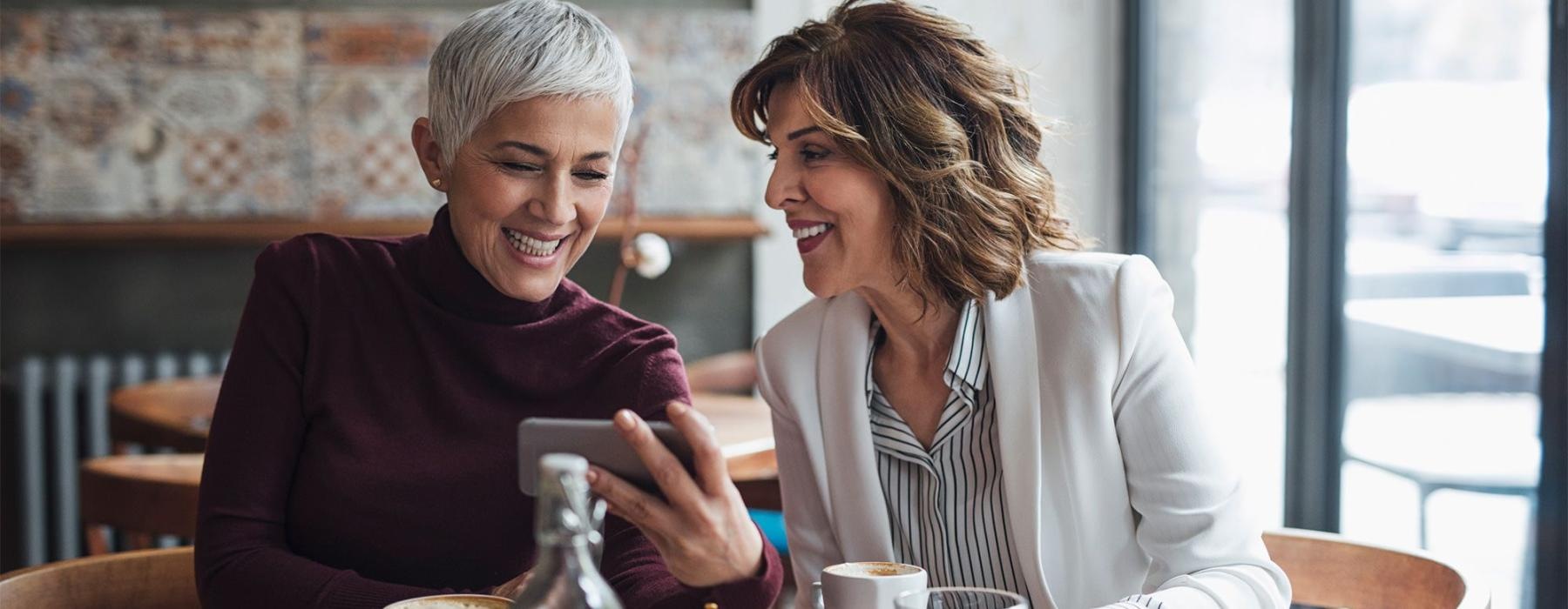 two women sitting at a table looking at a phone