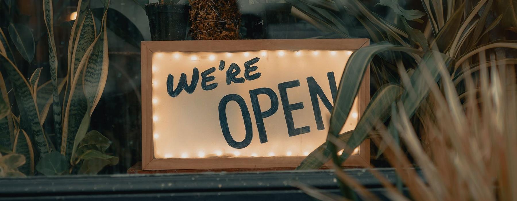 We're Open sign on a window ledge, surrounded by plants near brand new apartments in Dayton Ohio